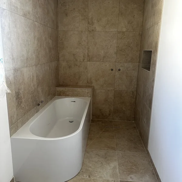 Salle de bain avec carrelage effet travertin beige et baignoire blanche