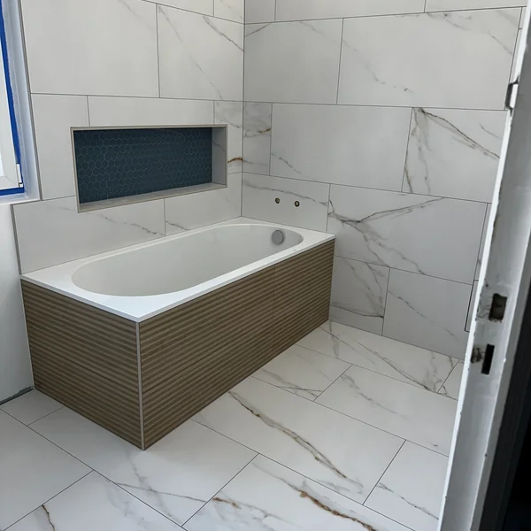 Salle de bain effet marbre blanc avec niche mosaïque et façade baignoire bois